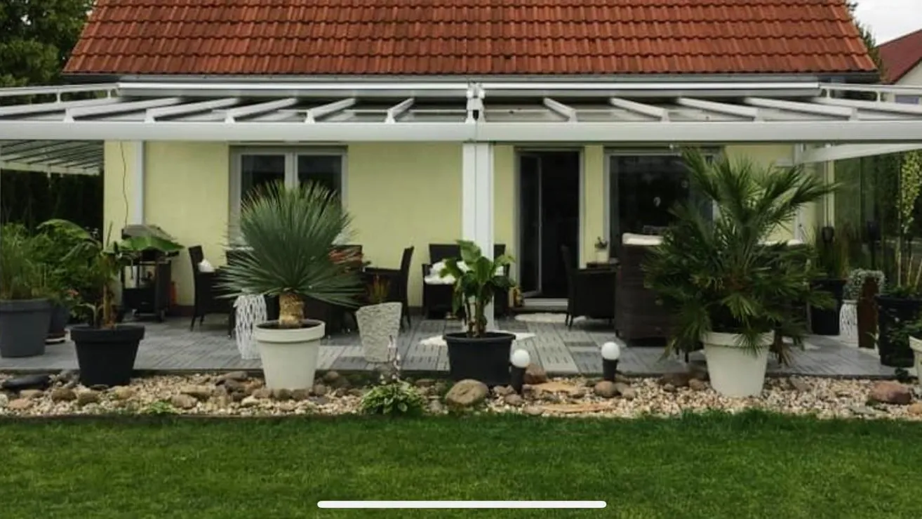 Weiße Terrassenüberdachung mit Glasdach an einem Einfamilienhaus