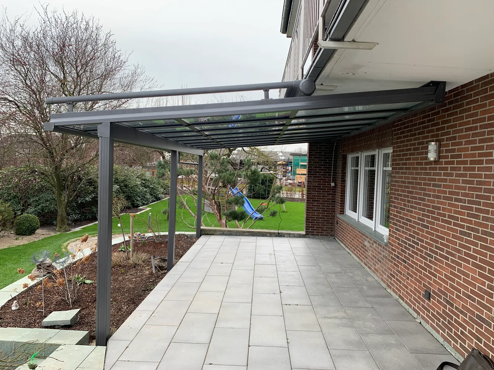 Anthrazitfarbenes Aluminium-Terrassendach an Klinkerwand